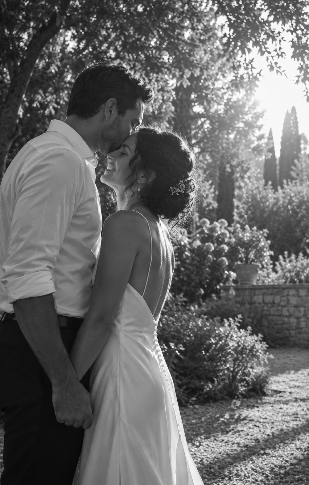 Un couple partage un baiser sur le front dans un jardin, en noir et blanc