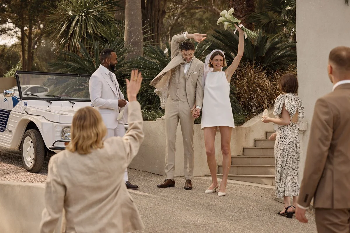 sortie des mariées avec une homme en costume beige et une femme en robe courte blanche