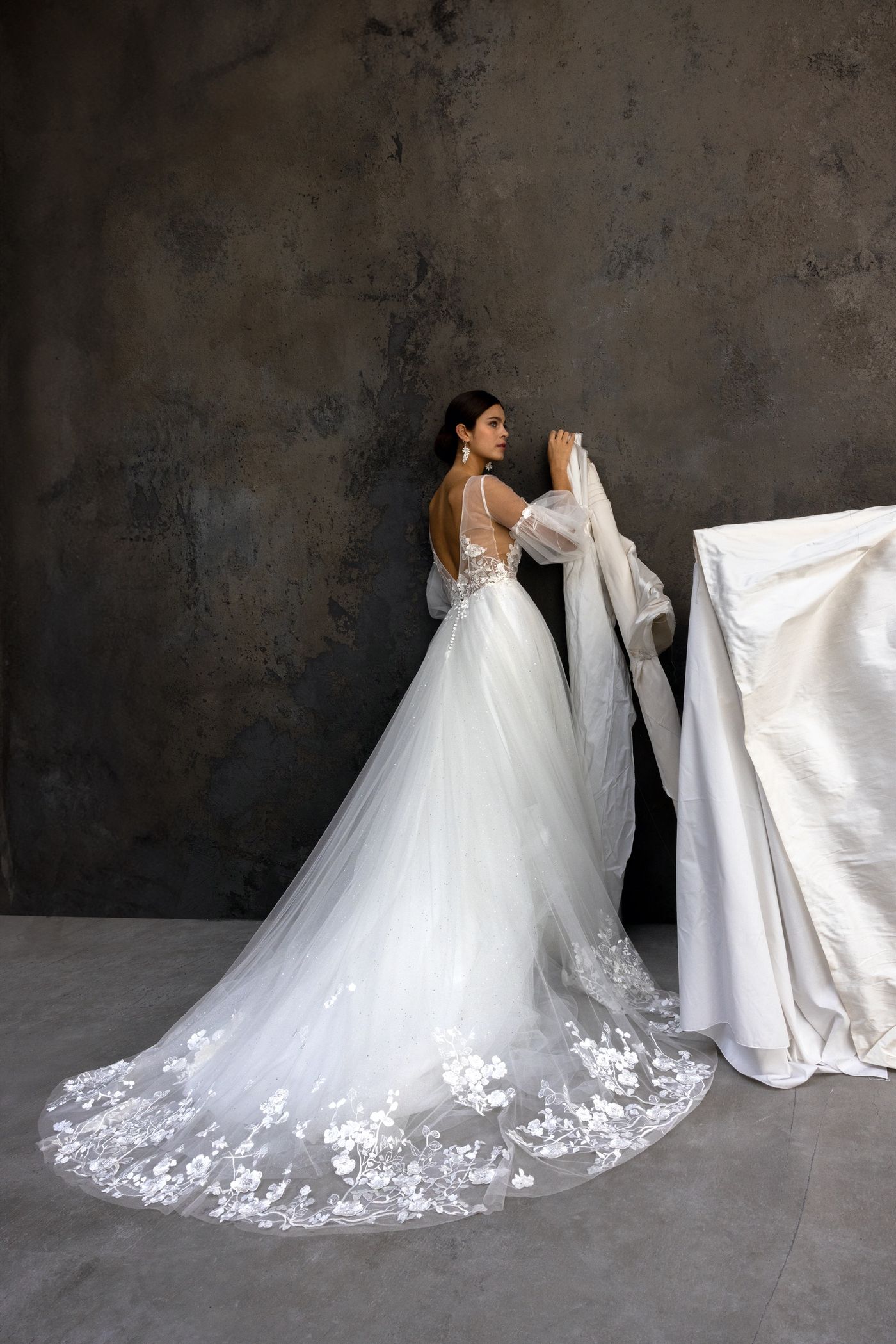 Une robe de mariée princesse 2025 en tulle pailleté à manches amovibles. Le décolleté à bretelles effet illusion est parsemé d’incrustations de tulle brodé aux motifs fleuris.